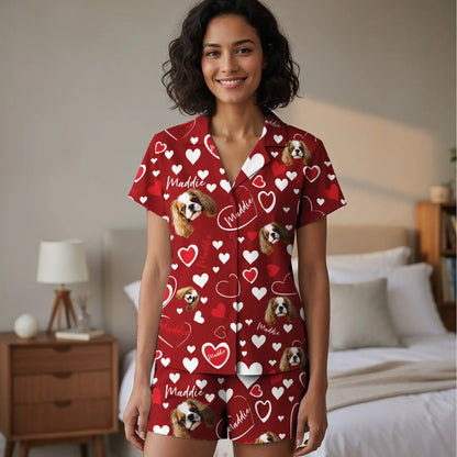 Photograph of a smiling, curly-haired woman in red pajamas with heart and dog patterns, standing in a beige bedroom.
