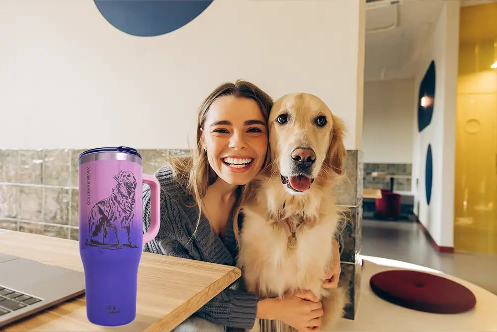 Photograph of a smiling young woman with light brown hair, wearing a gray sweater, sitting at a wooden table with a golden retriever. They are next to a purple mug with a lion design, in a modern, brightly lit cafe. Laptop and red plate are on the table.
